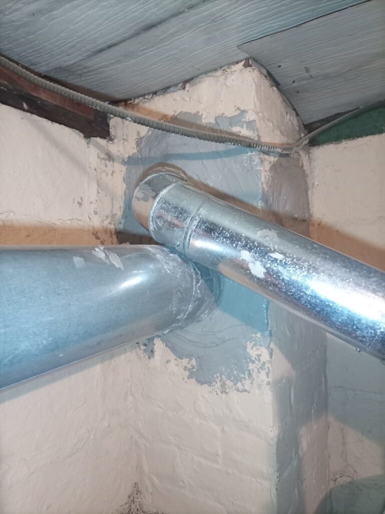 Metal pipe connection at the chimney in a basement utility area, Jersey City, NJ