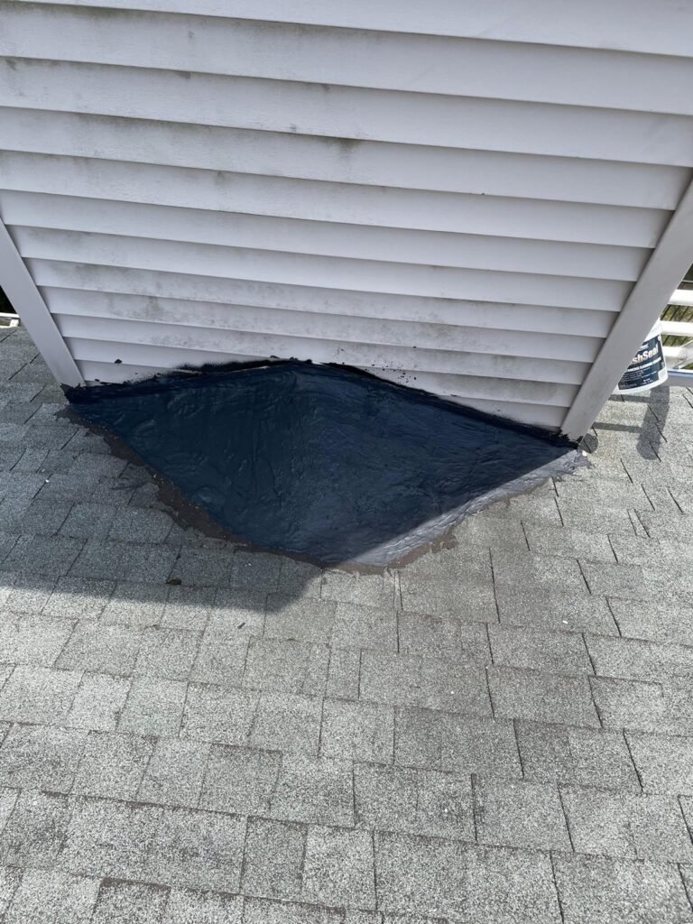 New black flashing material at the base of a vinyl-sided chimney chase where it meets the shingles