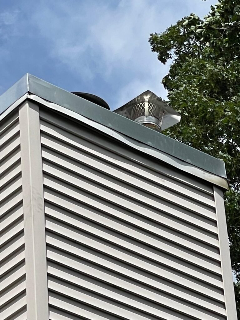 Metal pan and cap at the top of a vinyl-sided chimney chase