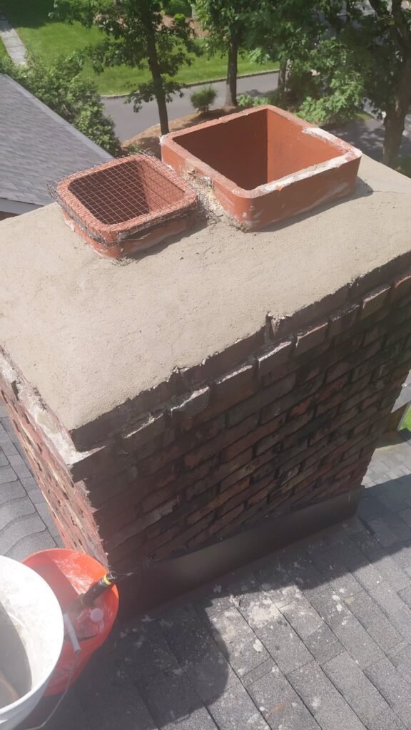 Brick chimney with two open clay flue tiles on a worn cement crown, before caps were fitted