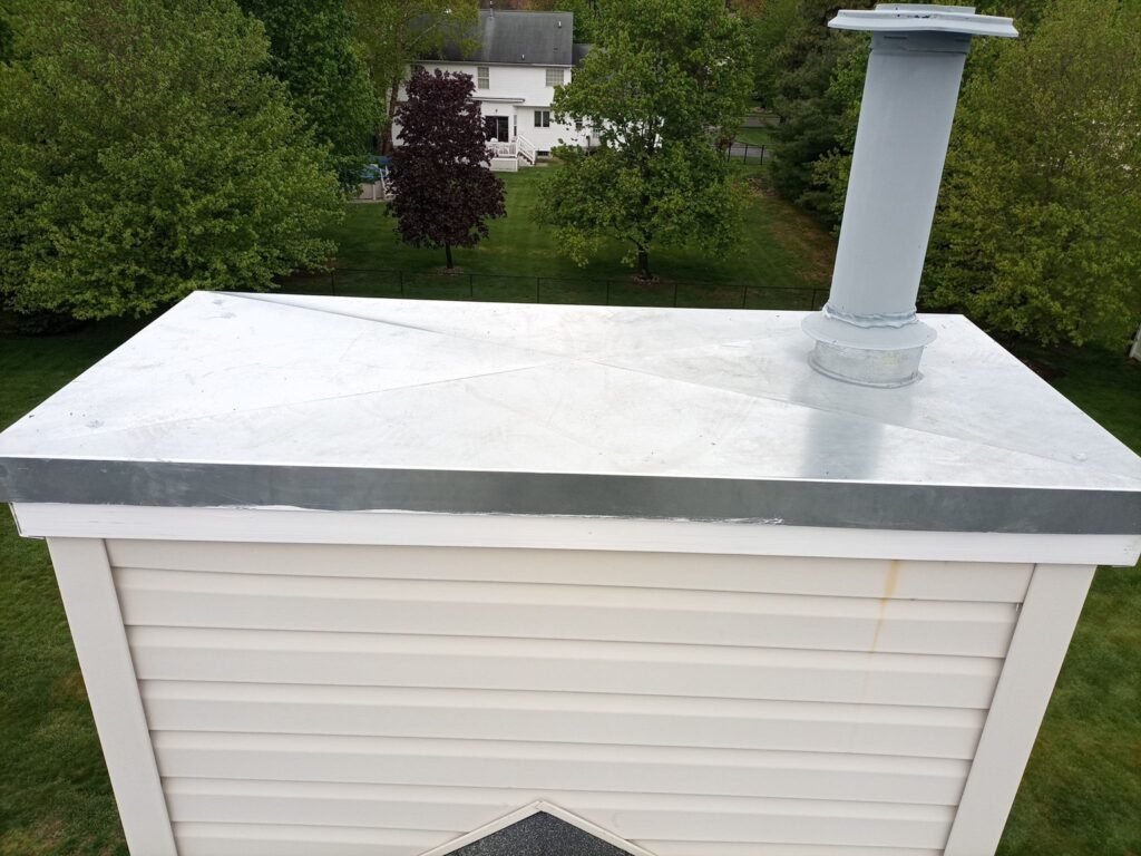 New metal chase cover with a flue pipe on a vinyl-sided chimney chase