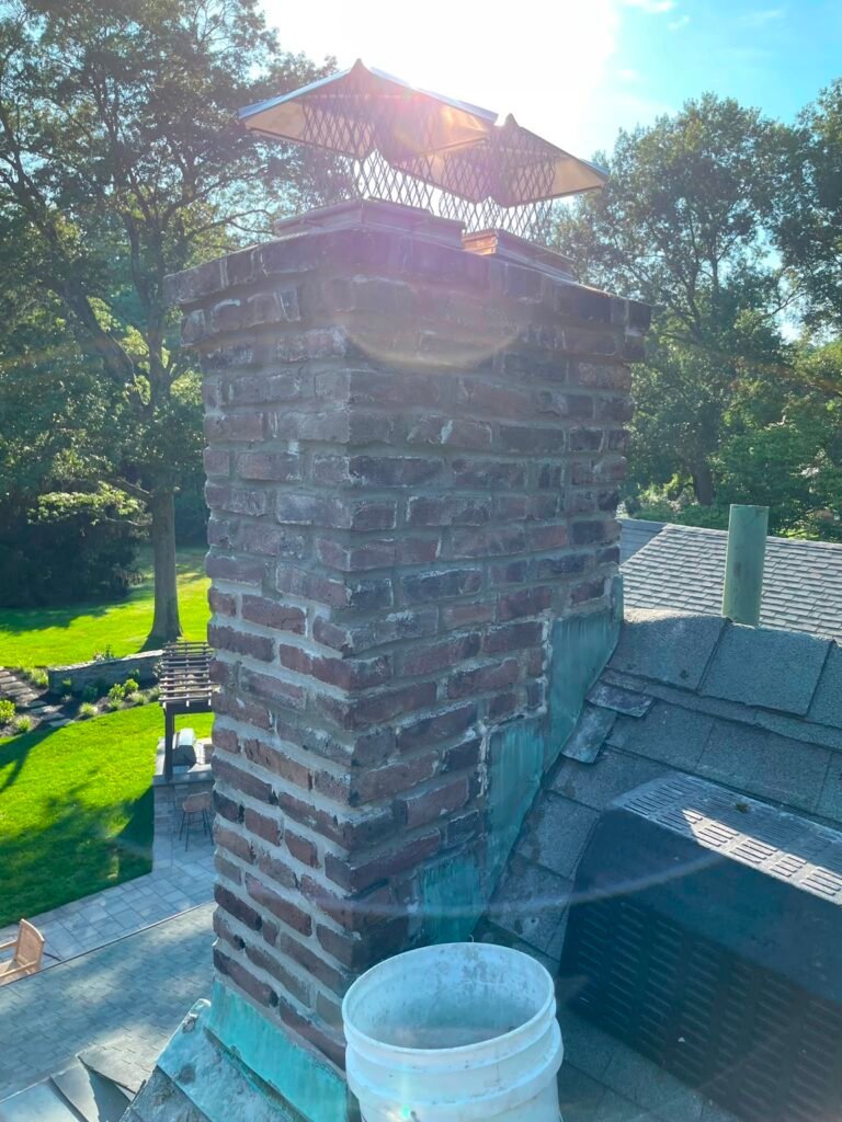 Weathered brick chimney beside a green copper-colored roof