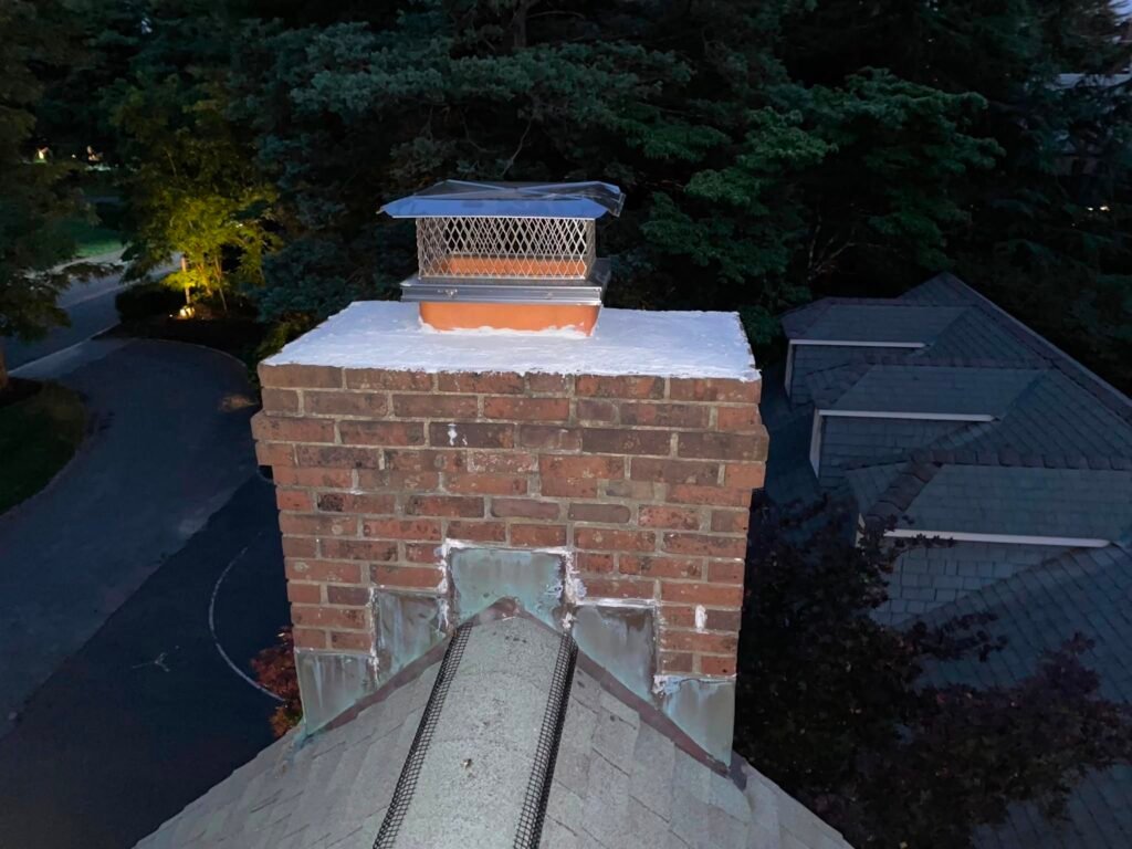 Brick chimney with a white-coated crown and a cap, aerial view at dusk