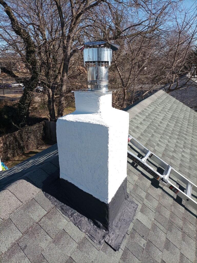 Finished white stucco chimney with a metal flue cap, seen from above the roof