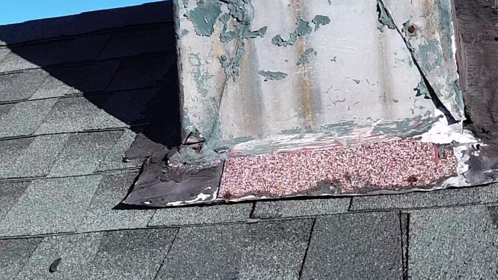 Peeling paint and worn flashing at the base of the chimney where it meets the shingles