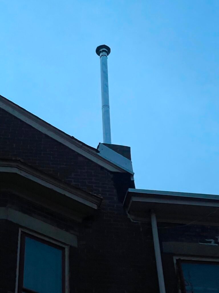 Brick chimney base with a new metal flue pipe and cap above the roofline